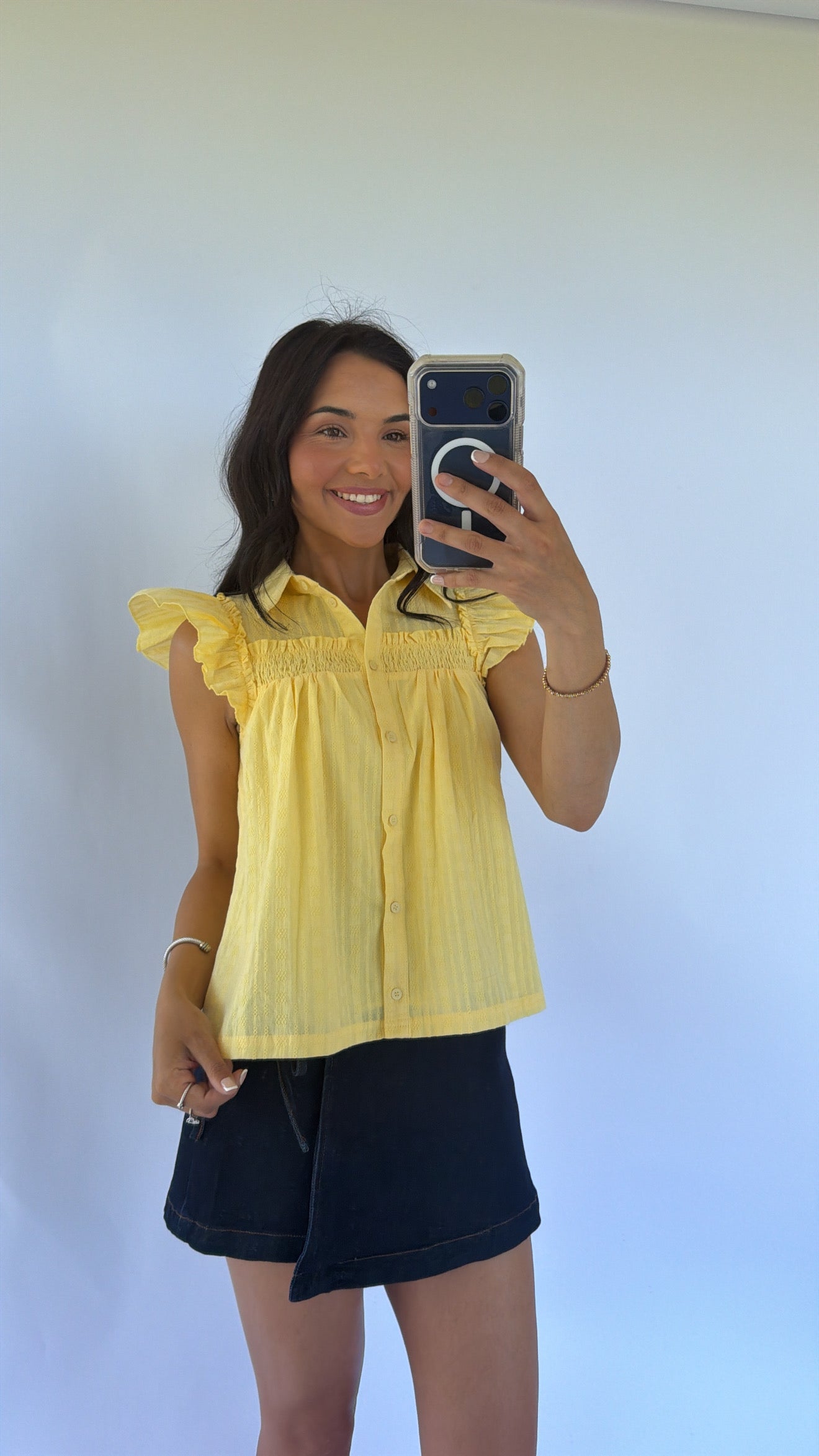 Woman taking a selfie wearing a yellow top and black shorts against a white background