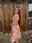 Woman in a floral dress standing in front of a wooden gate